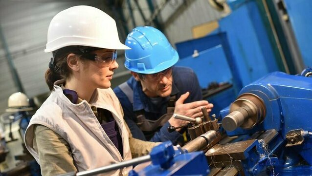 zwei Personen mit Helm bedienen eine Drehmaschine