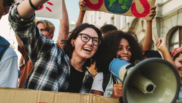 Zwei Frauen stehen in einer Gruppe Demonstrierenden und halten Schilder und ein Megaphon hoch.